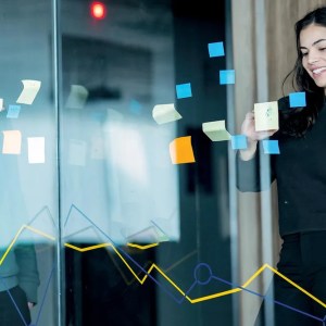 Temporada de balanços, Lucro líquido da Yduqs (YDUQ3) cai 80% no 3º tri com aumento de despesas financeiras, Mulher de pé mexe em post-its colados sobre vidro