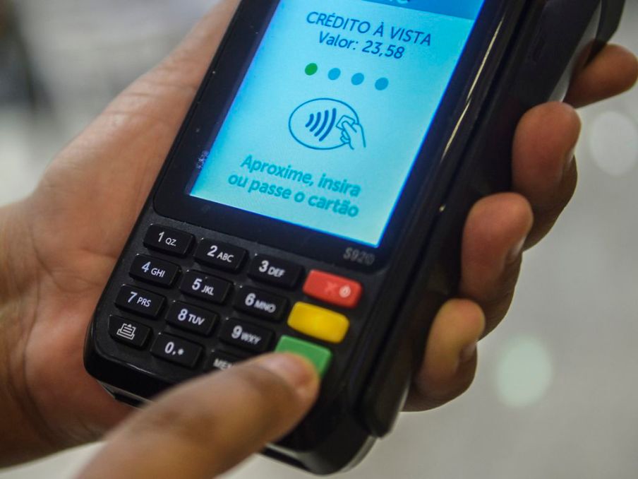 Foto de uma máquina de cartão de débito e crédito. Na tela, está escrito: "crédito à vista. Valor: 23,58"