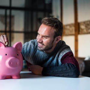 Imagem para o texto sobre quanto rendem R$ 200 mil na poupança em que está um homem colocando moedas em um cofrinho de porco cor de rosa.