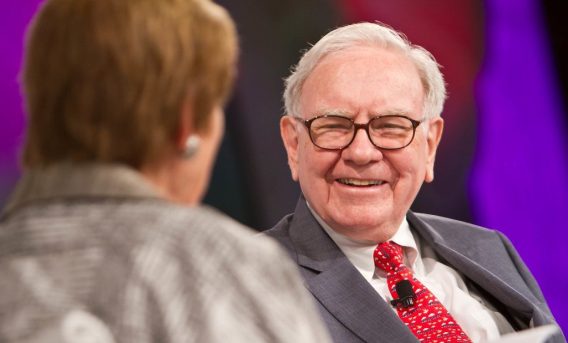 Foto de Warren Buffett, megainvestidor americano e dono da Berkshire Hathaway. Ele é branco, usa óculos, tem cabelos brancos e sorri à câmera.