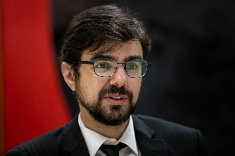 Foto de Guilherme Mello, secretário da Fazenda. Ele usa óculos, tem barba e veste terno.