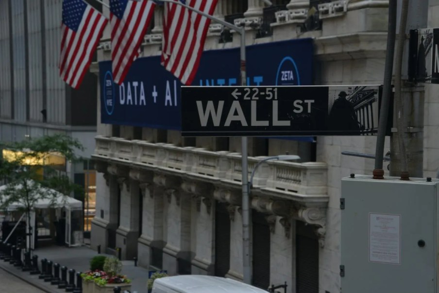 Imagem da fachada da Bolsa de Nova York, em Wall Street, com algumas bandeiras dos Estados Unidos.