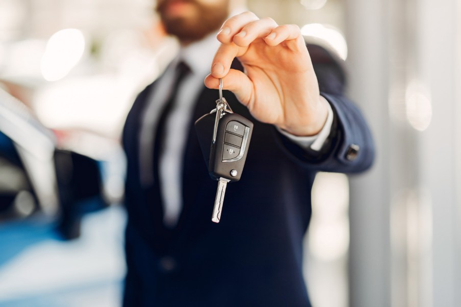 Imagem para o texto sobre como comprar o primeiro carro e como comprar uma casa em que aparece um homem de terno segurando uma chave de um automóvel.