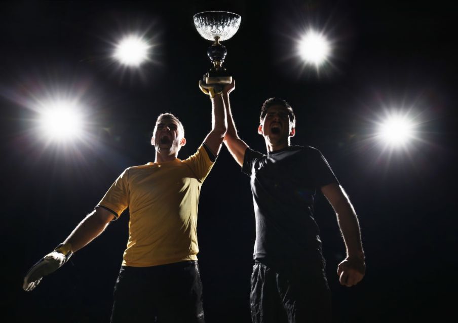 Imagem para o texto sobre os prêmios do futebol em que aparecem dois jogadores homens segurando uma taça