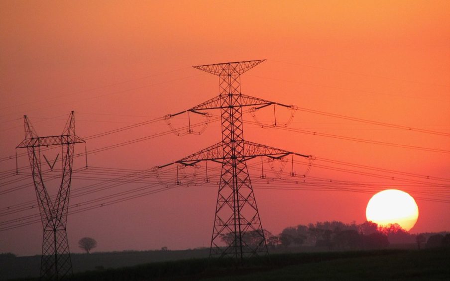 Foto de duas torres de transmissão de energia elétrica com um pôr-do-Sol ao fundo. A matéria explica previsões de dividendos da Taesa (TAEE11) para 2024 e 2025