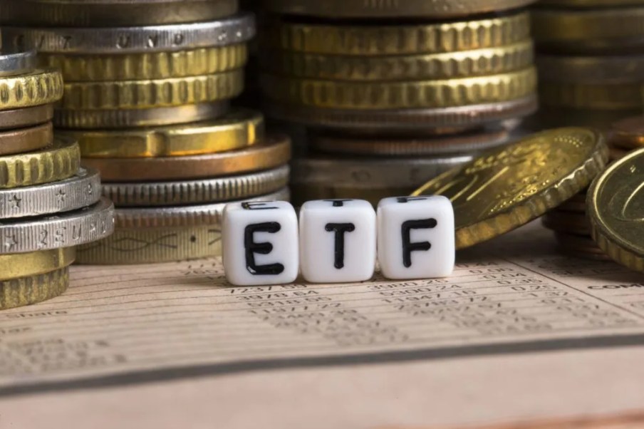 Imagem para o texto sobre alugar ETF em que aparecem em destaque três dadinhos com as letras E T F. Atrás, pilhas de moedas.