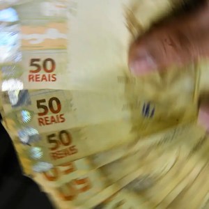Foto de uma mão em movimento segurando cédulas de R$ 50. A matéria explica como consultar dinheiro esquecido no Sistema de Valores a Receber, do Banco Central