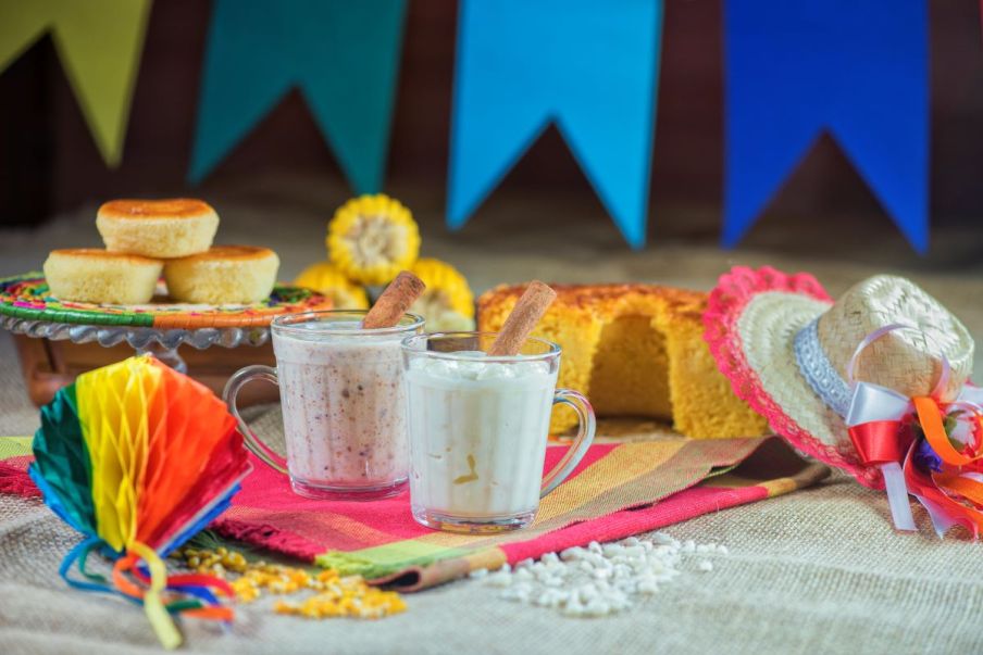 Imagem para matéria sobre comidas de festa junina em que aparece uma mesa com várias comidas, como bolo, espiga de milho, canjica, entre outros.