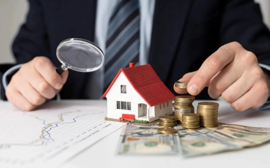 Foto de uma pessoa com uma lupa na mão esquerda e moedas na mão esquerda, com uma casa no meio. A matéria fala sobre onde investir em fundos imobiliários (FIIs) para 2025, com melhores recomendações.