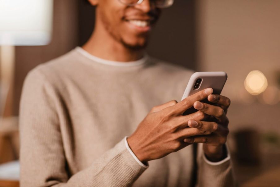 Imagem para matéria sobre o Superapp do Itaú Unibanco em que aparece um homem negro com uma blusa de manga bege sorrindo e segurando um celular.