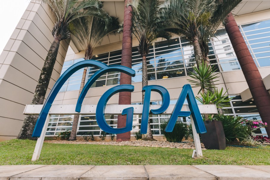 Foto de logo do Grupo Pão de Açúcar (PCAR3) azul sob fundo com prédio sede da varejista.