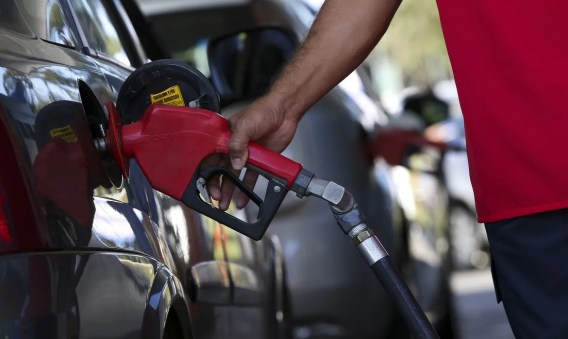 Imagem de uma mão segurando uma bomba de combustível sendo colocada no carro.