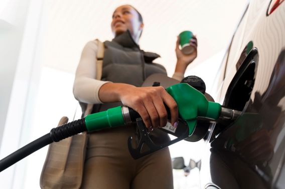 Imagem para matéria sobre gasolina e etanol em que aparece uma mulher negra colocando combustível em seu carro e segurando um copo de café.