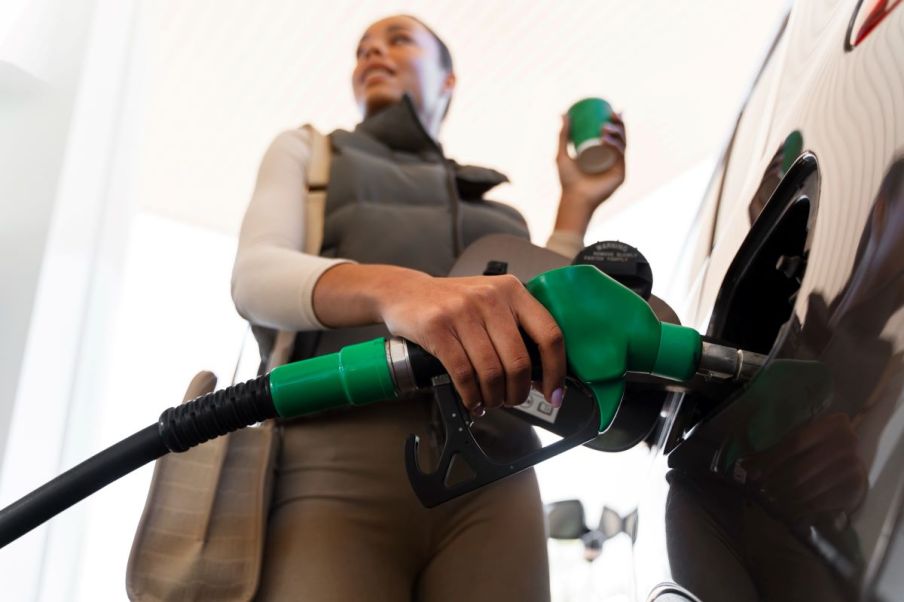 Imagem para matéria sobre gasolina e etanol em que aparece uma mulher negra colocando combustível em seu carro e segurando um copo de café.