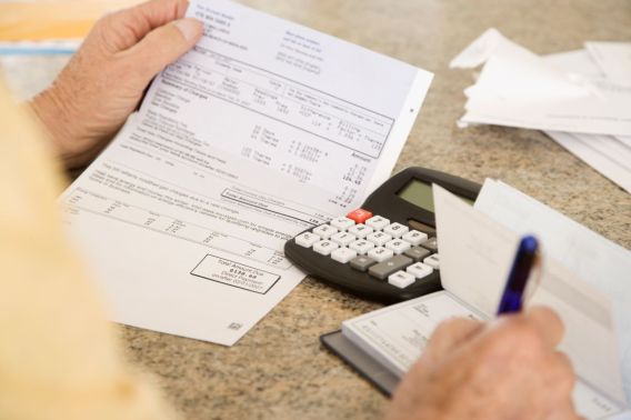 Foto de uma mão segurando um papel branco. Ao lado há uma calculadora.