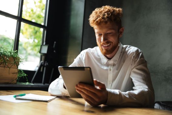 Foto de um jovem ruivo, vestindo uma camisa branca. Ele está segurando e olhando para um tablet.