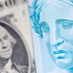 Foto de uma nota de dólar à esquerda e de uma cédula de cem reais à direita, em justaposição, para retratar matéria de previsões de dólar para cotação em real hoje do HSBC.